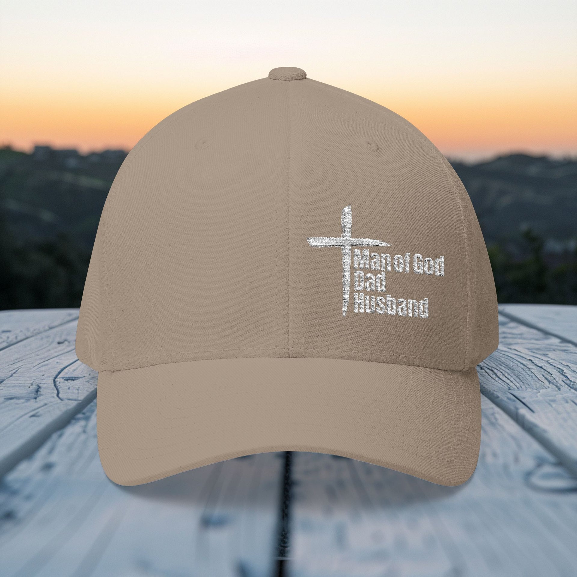 Man of God Dad Husband Embroidered Flexfit Hat displayed outdoors at sunset.