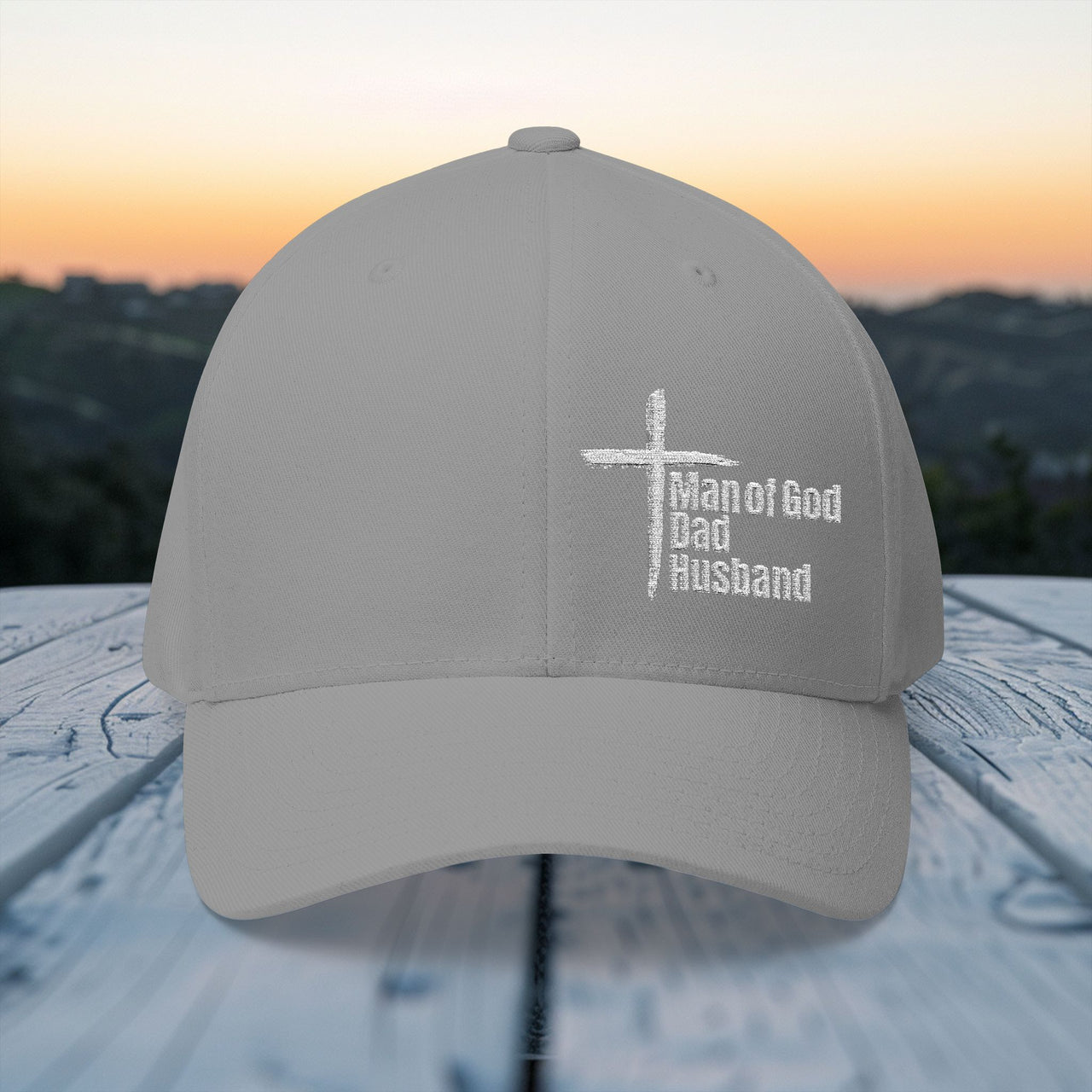 Man of God, Dad, Husband Embroidered Flexfit Hat displayed outdoors at sunset