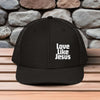 Love Like Jesus snapback hat on a wooden surface with stone background, promoting faith and style.