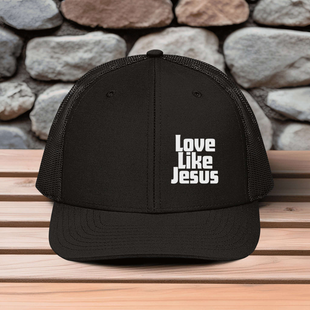 Love Like Jesus snapback hat on a wooden surface with stone background, promoting faith and style.