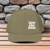 Love Like Jesus snapback hat displayed on a wooden table with a stone wall background.