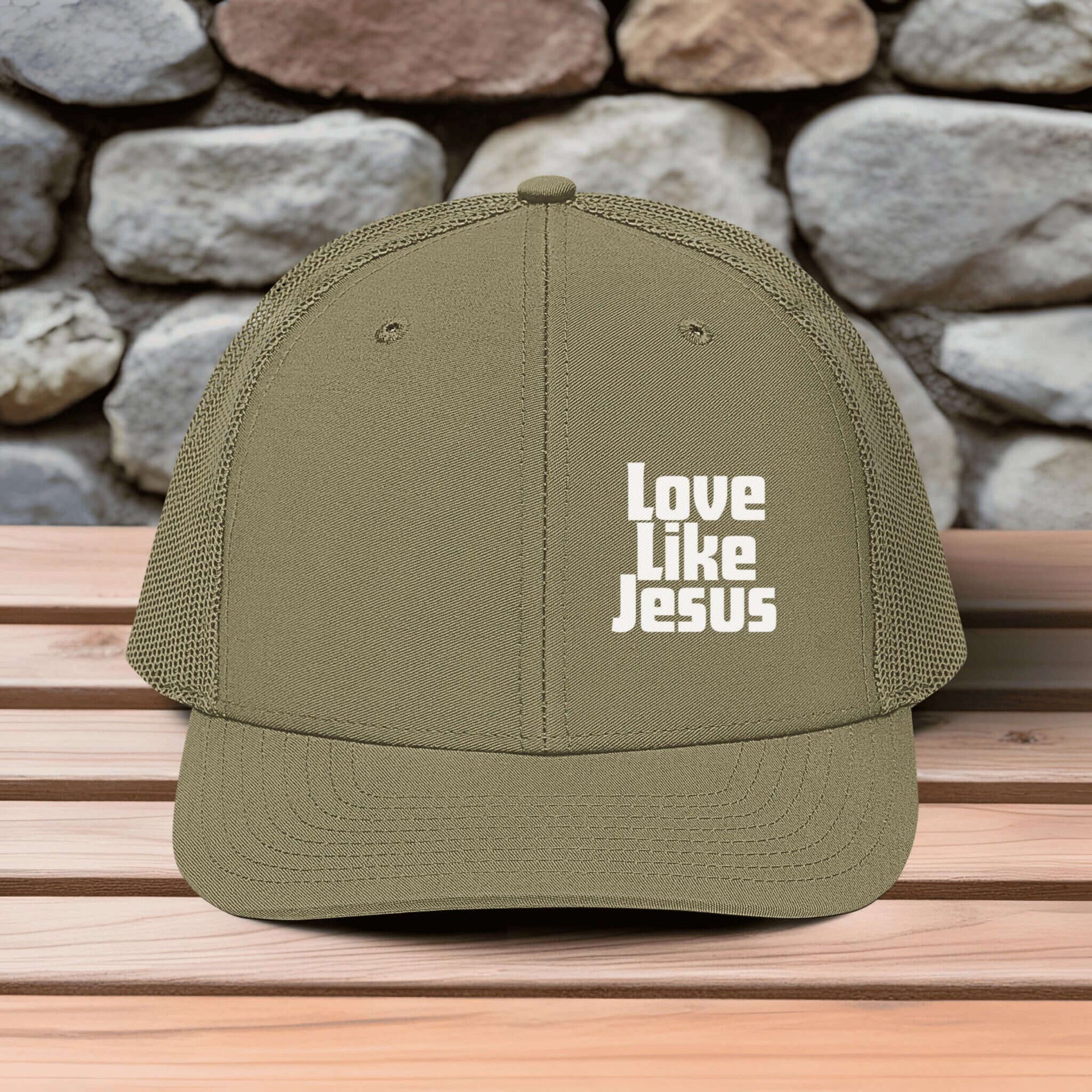 Love Like Jesus snapback hat displayed on a wooden table with a stone wall background.