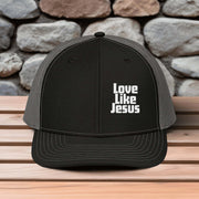 Love Like Jesus snapback hat displayed on a wooden surface with a stone background.