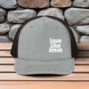 Love Like Jesus snapback hat displayed on a wooden surface with a stone backdrop, featuring bold embroidery.