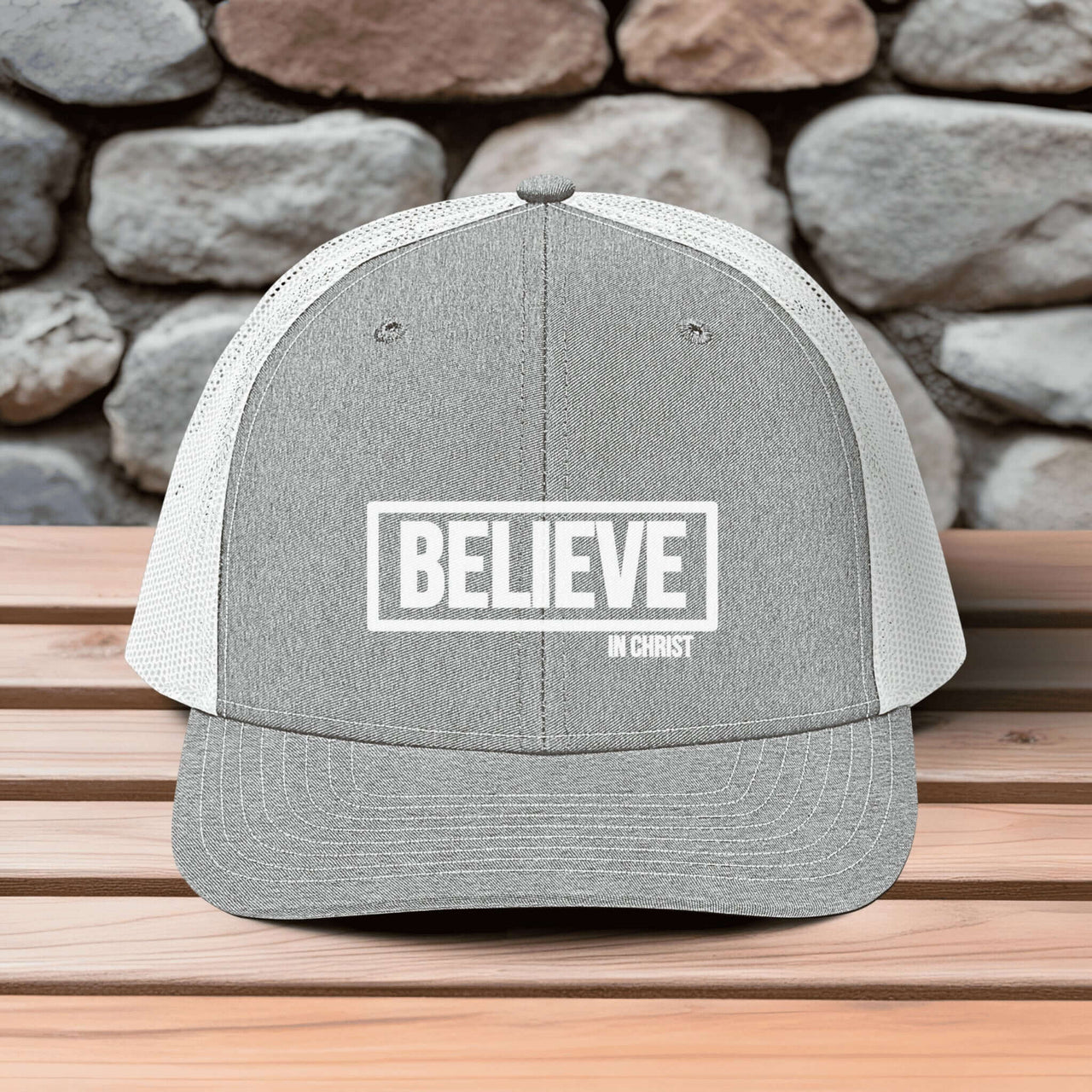 Believe In Christ Snapback Hat with embroidered design, set on wooden surface against a stone wall background.