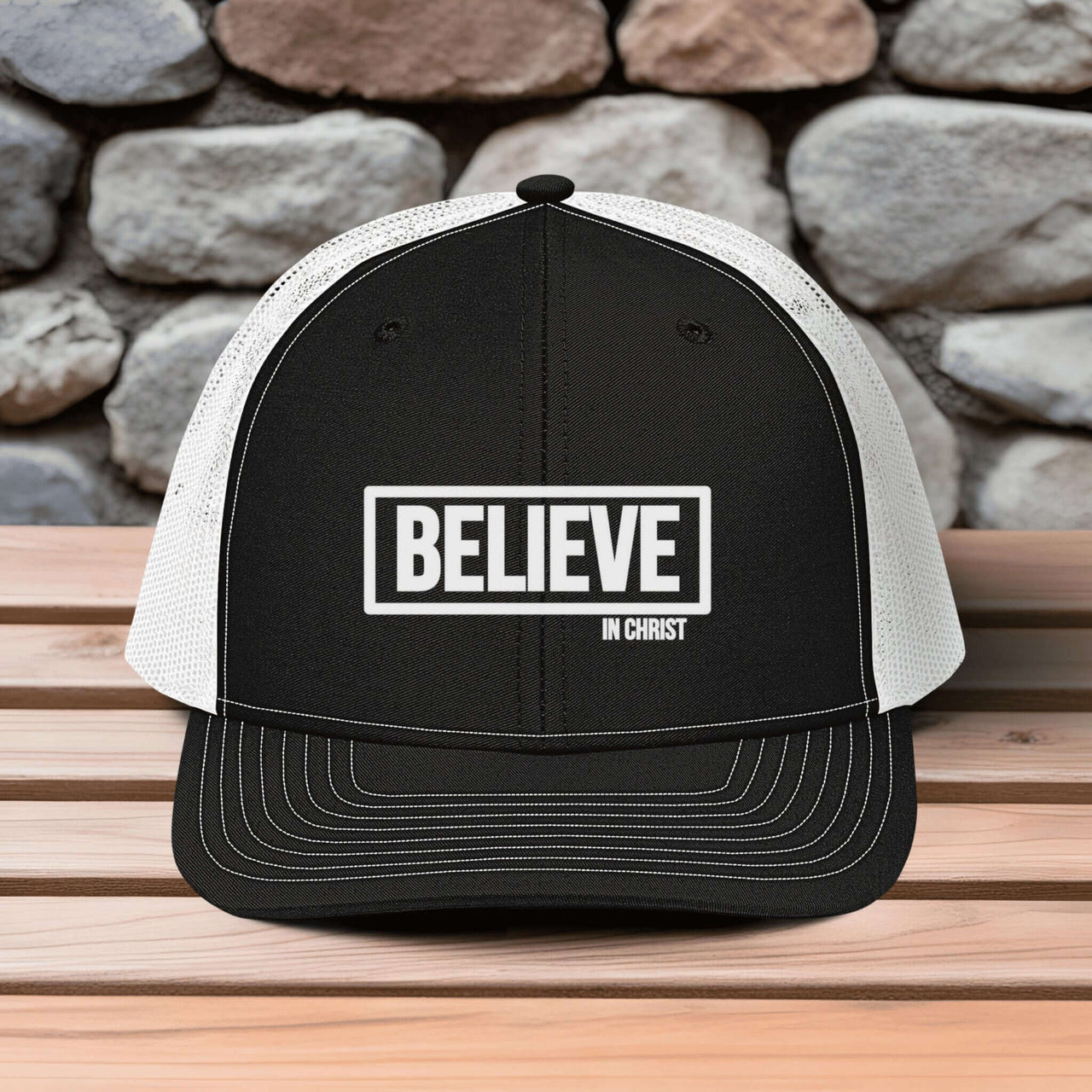 Believe In Christ Snapback Hat with embroidered design on a wooden table against a stone background.