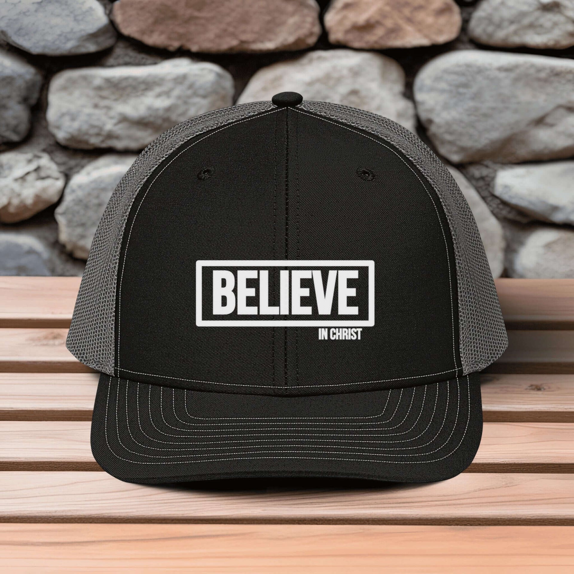 Believe In Christ Snapback Hat with embroidered design on a wooden table against a stone background.