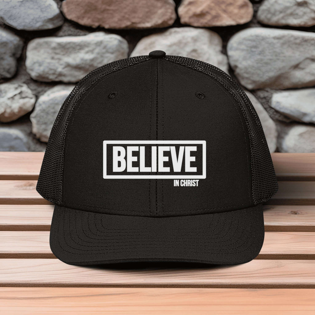 Believe In Christ Snapback Hat on a wooden surface with a stone wall background, showcasing an embroidered design.