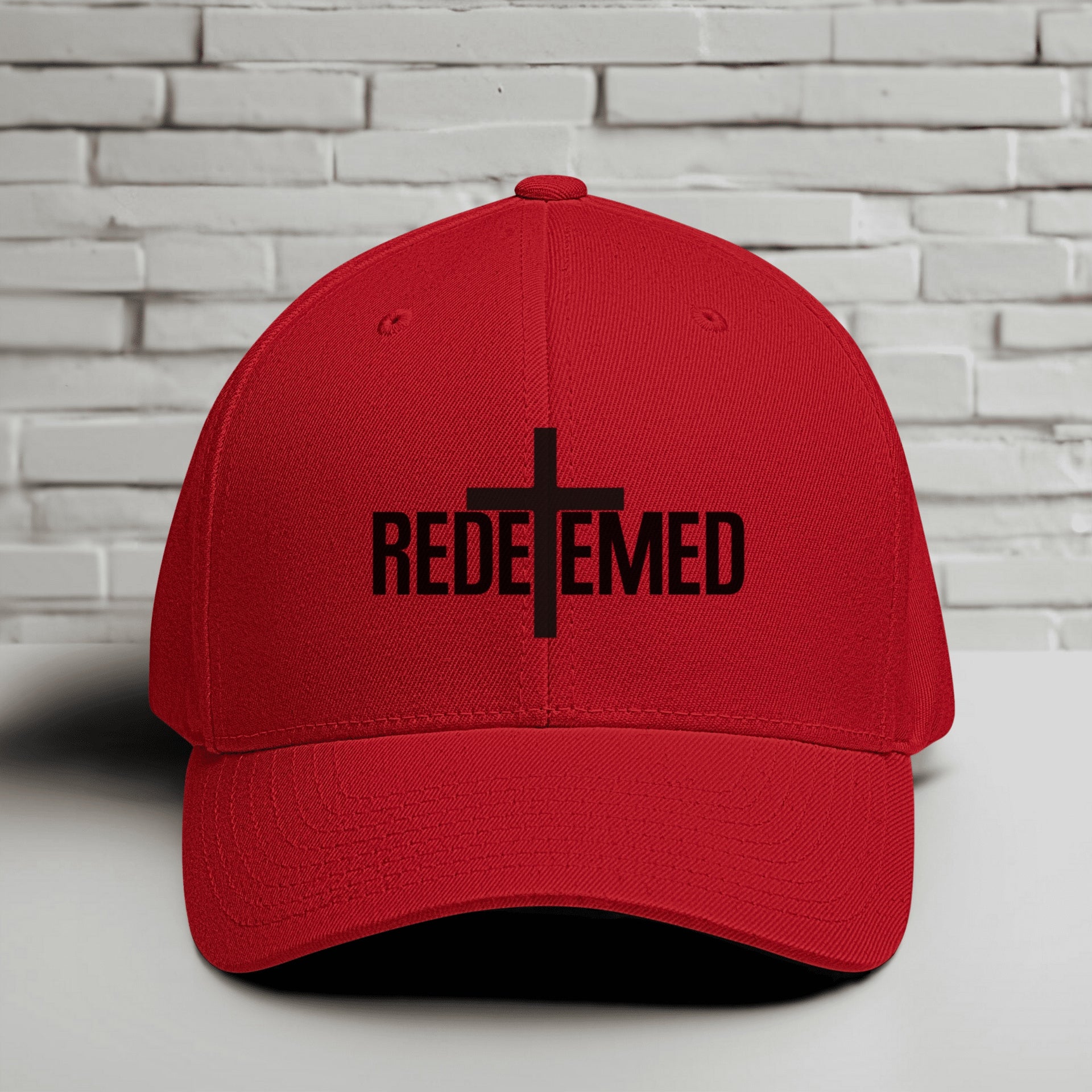 Redeemed Embroidered Flexfit Hat displayed against a brick background, symbolizing faith and identity.