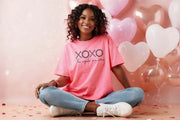 XOXO The Original Love Letters Tee Crown of Thorns Shirt worn by a smiling woman in a pink shirt with heart balloons.