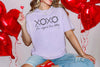 XOXO The Original Love Letters Tee Crown of Thorns Shirt worn by a woman surrounded by heart-shaped balloons.