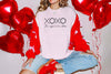 XOXO The Original Love Letters Tee Crown of Thorns Shirt worn by a model surrounded by heart balloons.