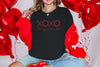 XOXO The Original Love Letters Tee Crown of Thorns Shirt worn by a model with red balloons in the background.