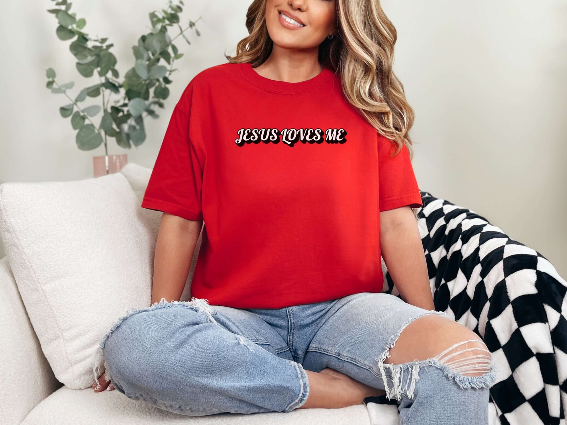 Jesus Loves Me Unisex T-shirt worn by a woman sitting on a couch, highlighting its comfortable style and faith-inspired design.