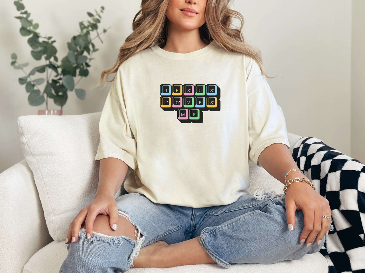Jesus Loves Me Unisex T-Shirt displayed on a model sitting on a couch, featuring a keyboard keys graphic.