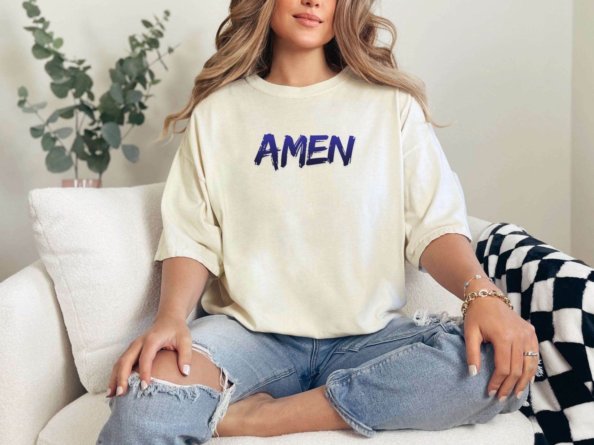 Amen Brush Stroke Unisex T-shirt worn by a woman sitting on a couch, featuring bold 'AMEN' text.