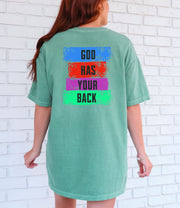 Back view of a woman wearing a God Has Your Back T-Shirt with color block lettering on a light green t-shirt.