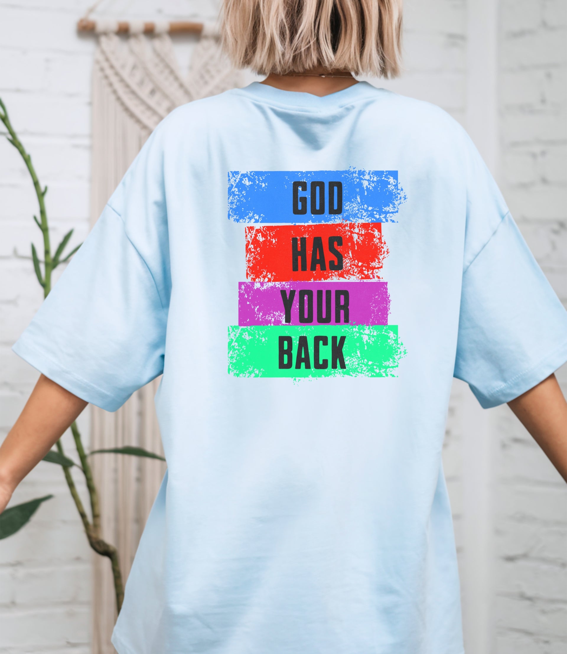 God Has Your Back T-Shirt featuring colorful block text on a chambray t-shirt, showcasing a bold and encouraging message.