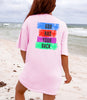 God Has Your Back T-Shirt in pink with colorful block design on beach, promoting confidence and peace.
