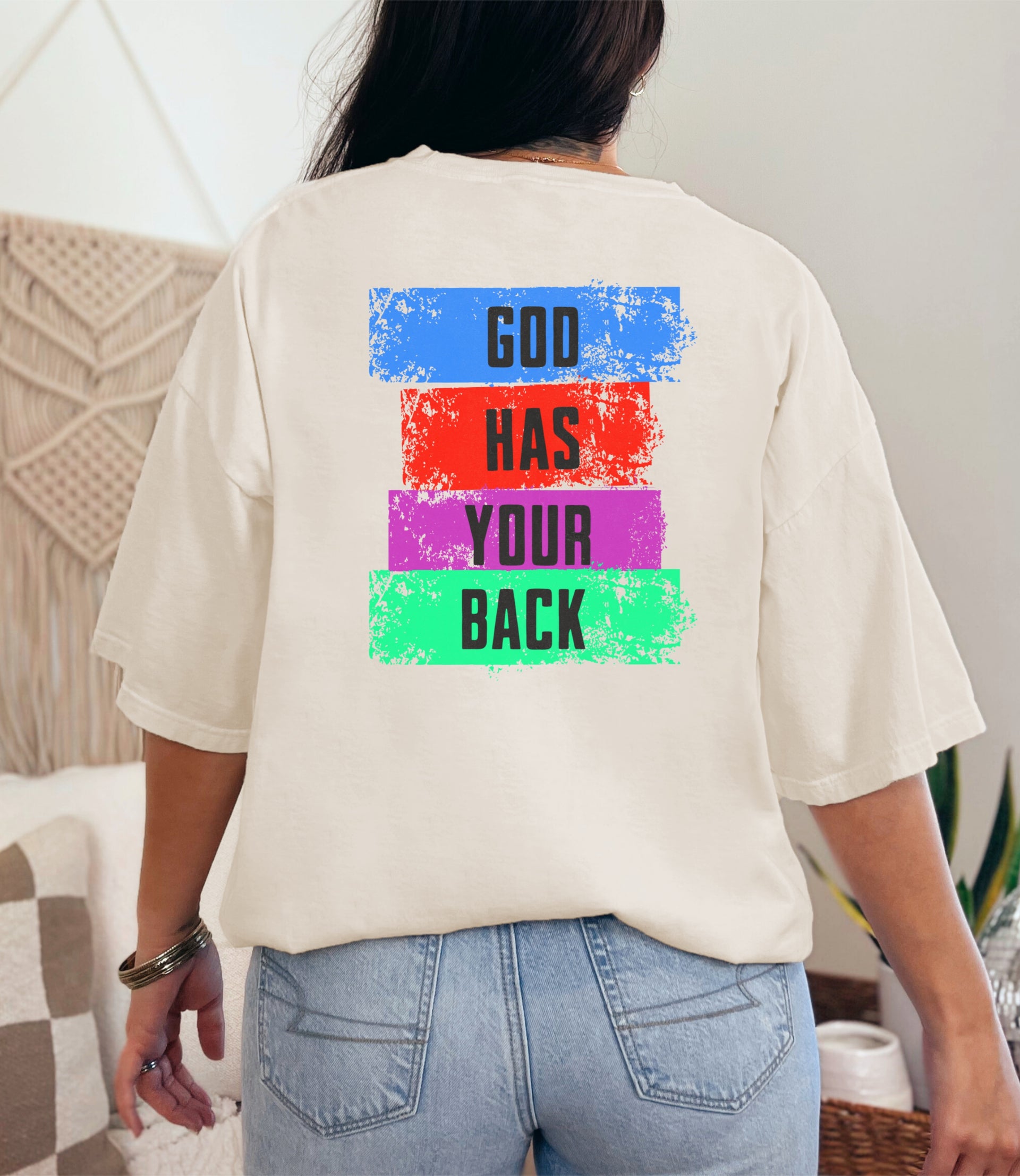 Girl wearing God Has Your Back T-Shirt with colorful block design on the back, showcasing an empowering message.