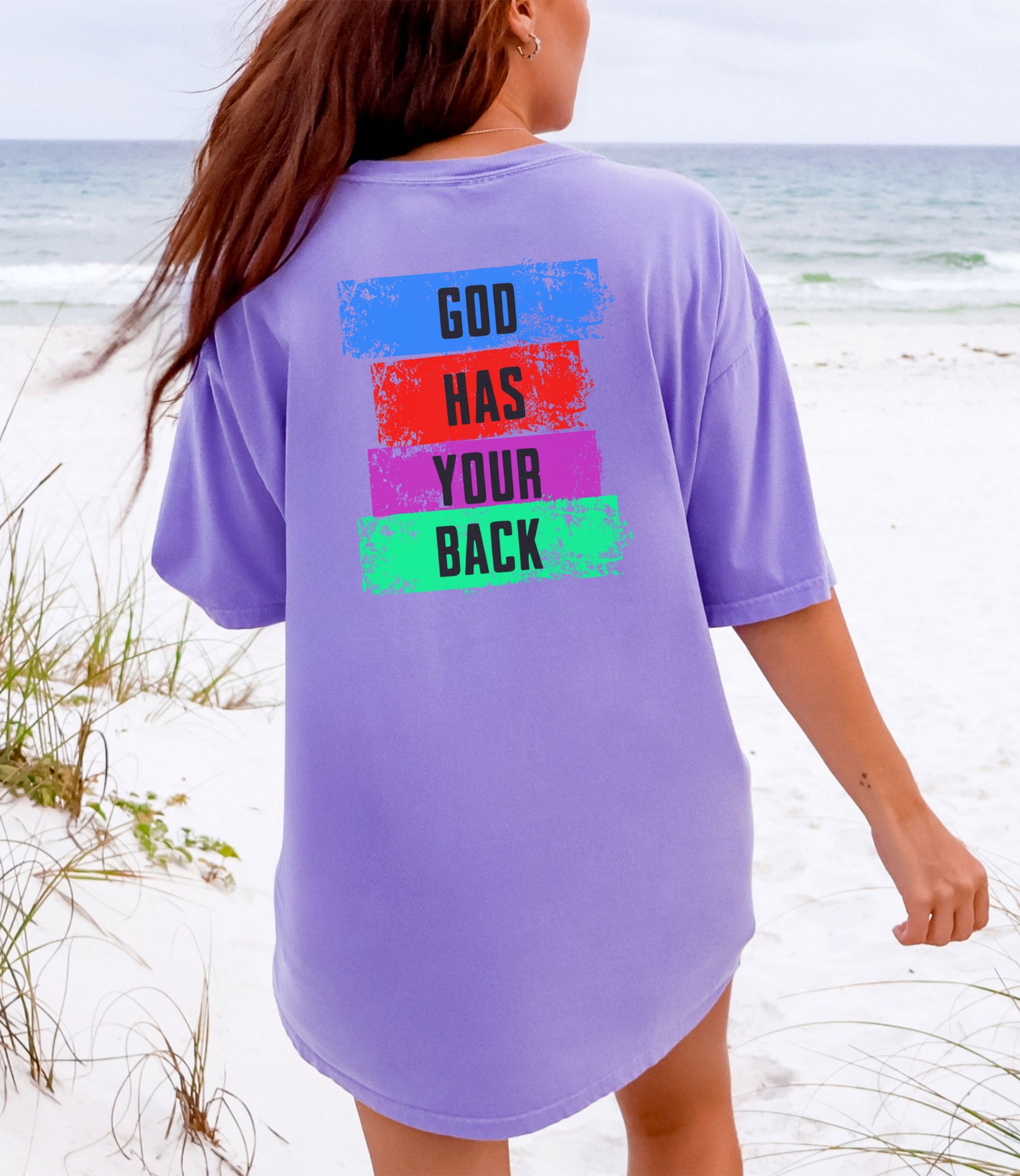 God Has Your Back T-Shirt displayed on a model by the beach with a vibrant color block design.