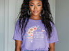 She Laughs Without Fear Of The Future Floral T Shirt displayed on a model with a floral design and purple background.