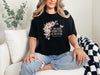 She Laughs Without Fear Of The Future Floral T Shirt displayed on a woman sitting on a couch with a floral design.