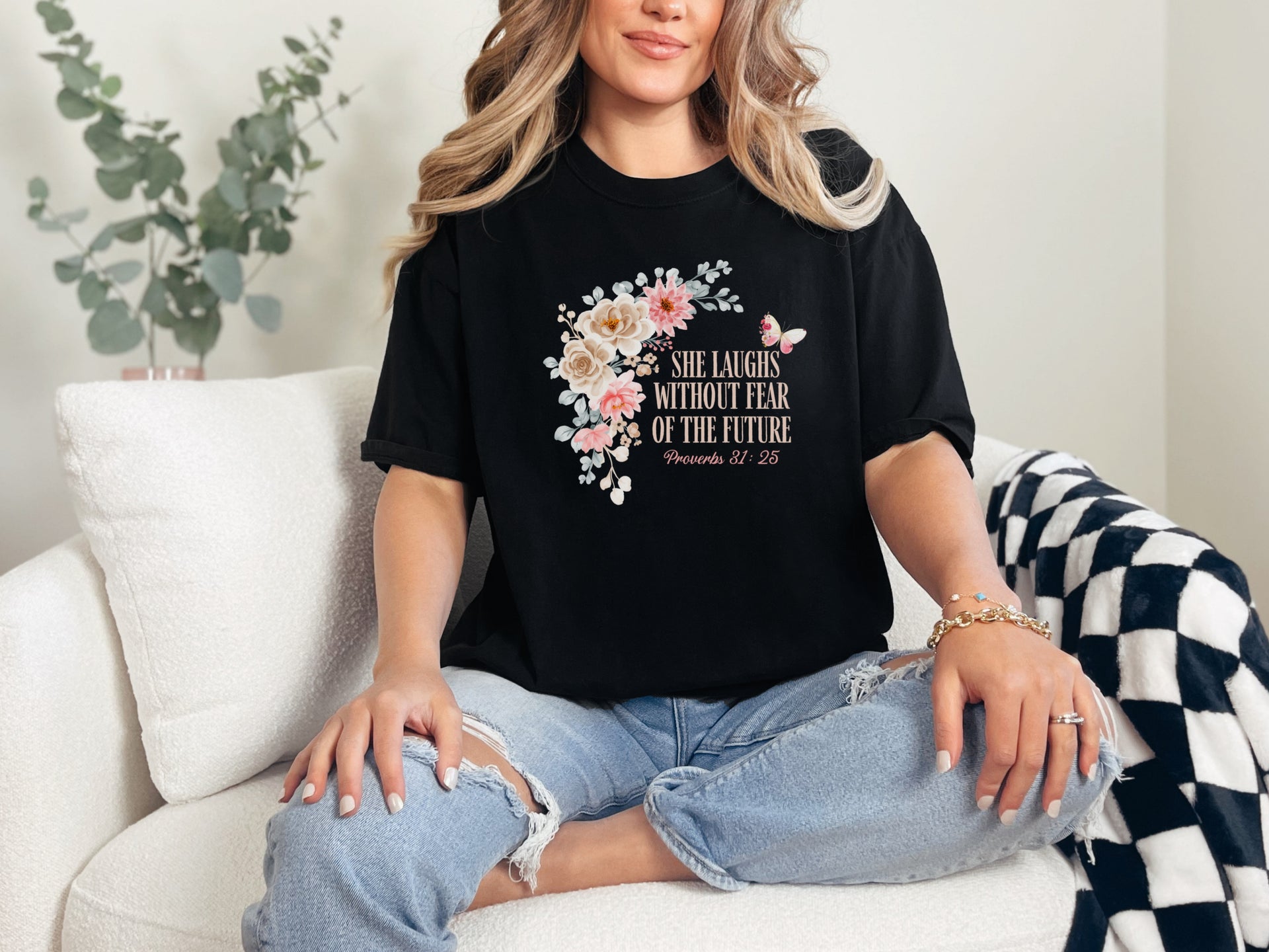 She Laughs Without Fear Of The Future Floral T Shirt displayed on a woman sitting on a couch with a floral design.