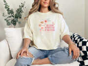 She Laughs Without Fear Of The Future Floral T Shirt worn by a woman sitting on a couch with a floral design.