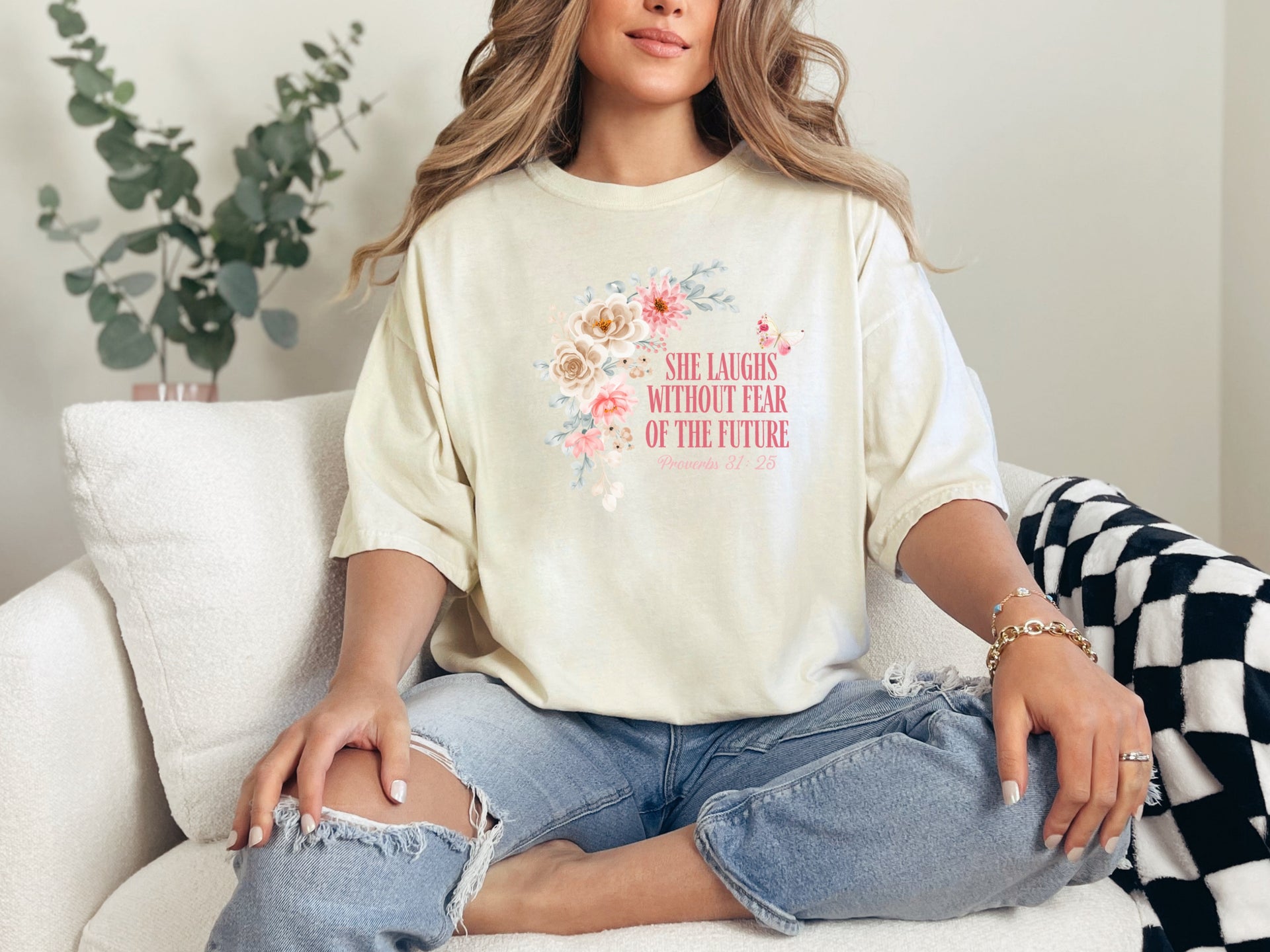 She Laughs Without Fear Of The Future Floral T Shirt worn by a woman sitting on a couch with a floral design.