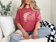 She Laughs Without Fear Of The Future Floral T Shirt worn by a woman with a floral design, sitting casually on a couch.