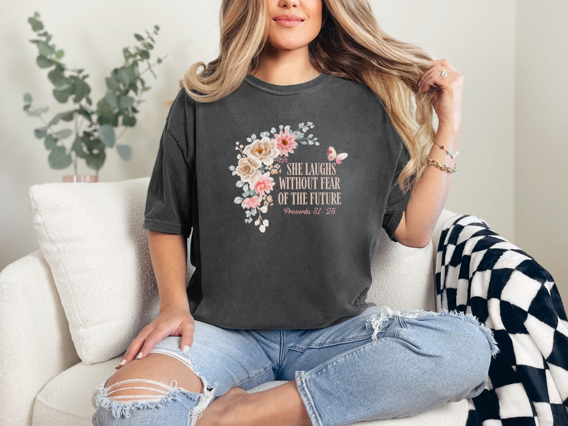 She Laughs Without Fear Of The Future Floral T Shirt worn by a woman sitting on a couch with floral design and Proverbs 31:25.