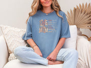 She Is Mom Floral Typography T Shirt worn by a woman sitting on a couch with soft fabric and a stylish design.