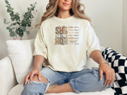 She Is Mom Floral Typography T Shirt worn by a woman, featuring a design that celebrates motherhood with floral typography.