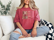 She Is Mom Floral Typography T Shirt worn by a woman in a cozy setting, showcasing the unique floral design.