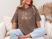 She Is Mom Floral Typography T Shirt worn by a woman sitting comfortably, showcasing a stylish floral design on a soft tee.