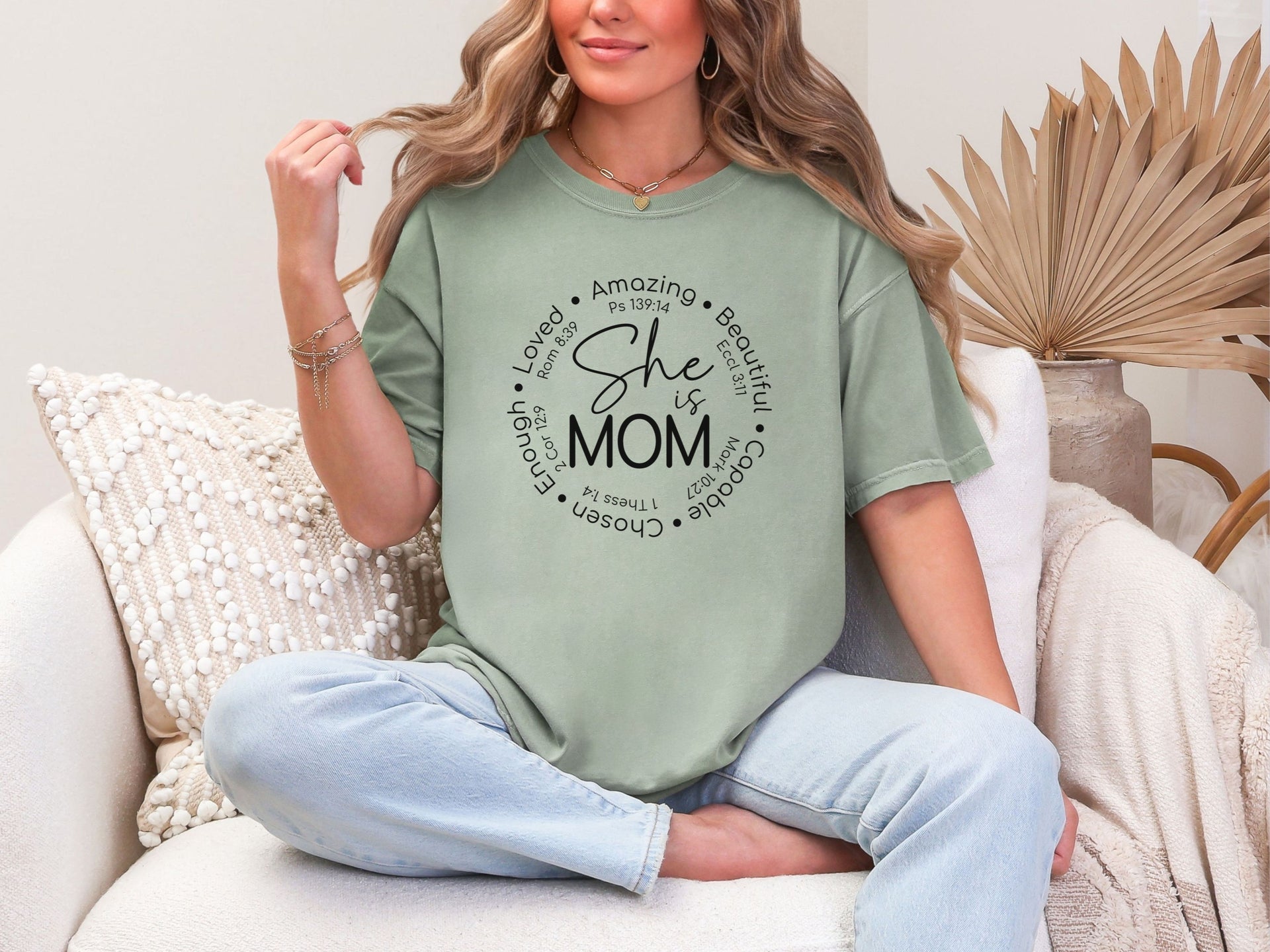 She Is Mom Circle Script T Shirt modeled by a smiling woman on a couch, showcasing its soft fabric and stylish design.