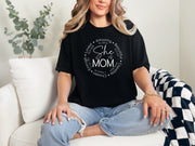 She Is Mom Circle Script T Shirt worn by a woman sitting and smiling, featuring a circular script design celebrating motherhood.