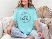 She Is Mom Circle Script T Shirt worn by a woman sitting on a couch, showcasing a soft blue color and circular script design.