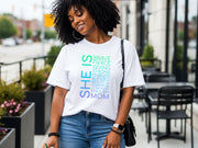 SHE IS vertical affirmation mom T-Shirt worn by a smiling woman outdoors, showcasing uplifting typography design.