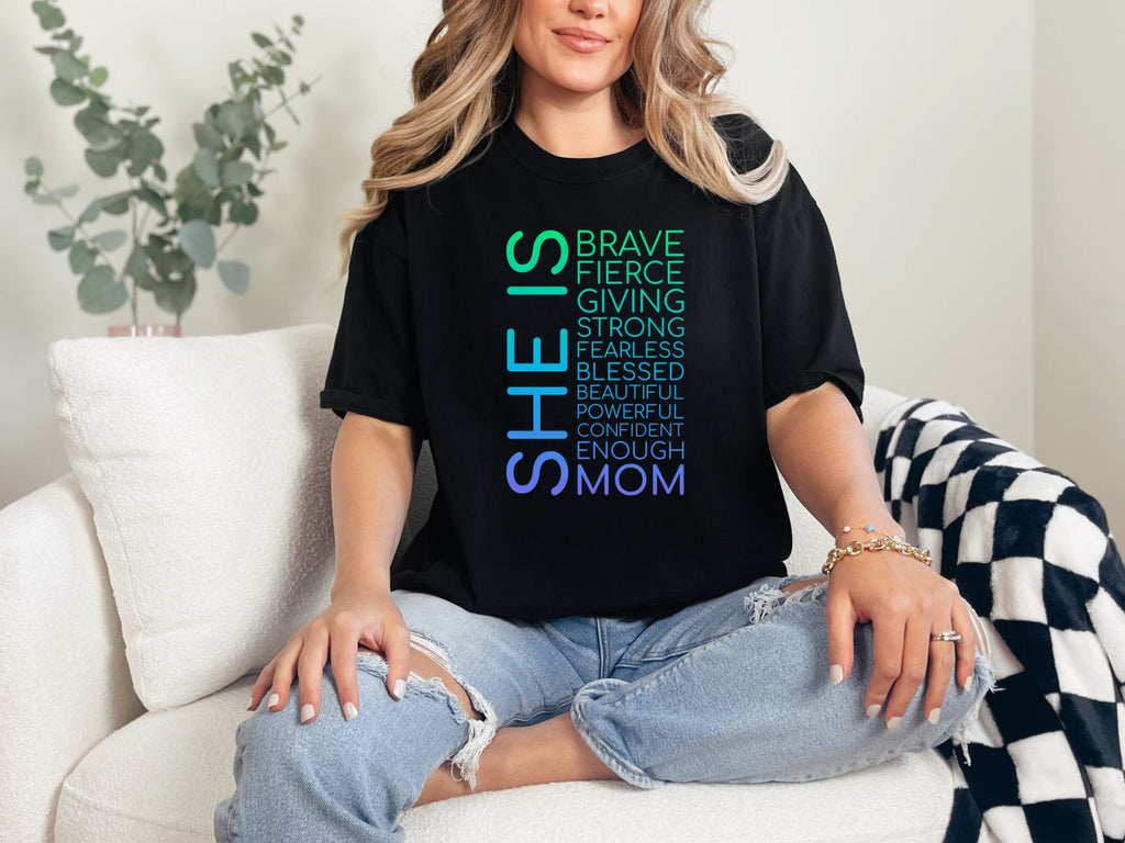 A woman wearing a SHE IS vertical affirmation mom T-Shirt with positive affirmations, showcasing strength in motherhood.