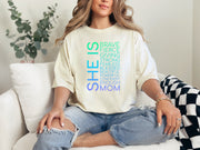Model wearing SHE IS vertical affirmation mom T-Shirt with uplifting words. Comfortably styled for everyday wear.