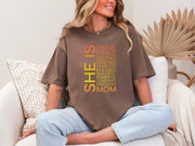 Model wearing SHE IS vertical affirmation mom T-Shirt with uplifting affirmations in vibrant colors.