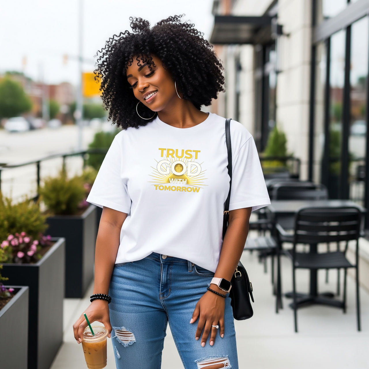 Woman wearing a Trust God With Tomorrow T-Shirt, enjoying a drink while walking in a city setting.