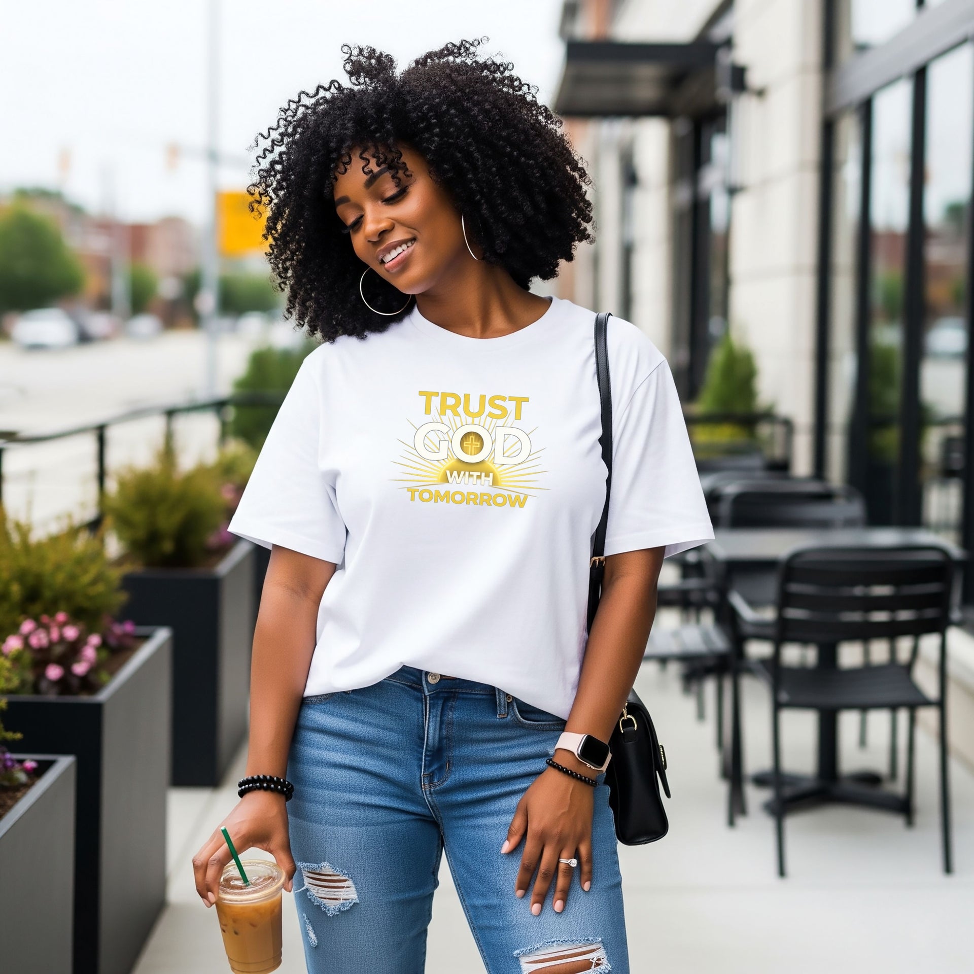 Woman wearing a Trust God With Tomorrow T-Shirt, enjoying a drink while walking in a city setting.