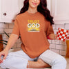 Woman wearing Trust God With Tomorrow T-Shirt, sitting casually in a kitchen with a coffee mug.