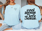 Model wearing a Cool Moms Love Jesus T Shirt featuring heart design and trendy font on the back.
