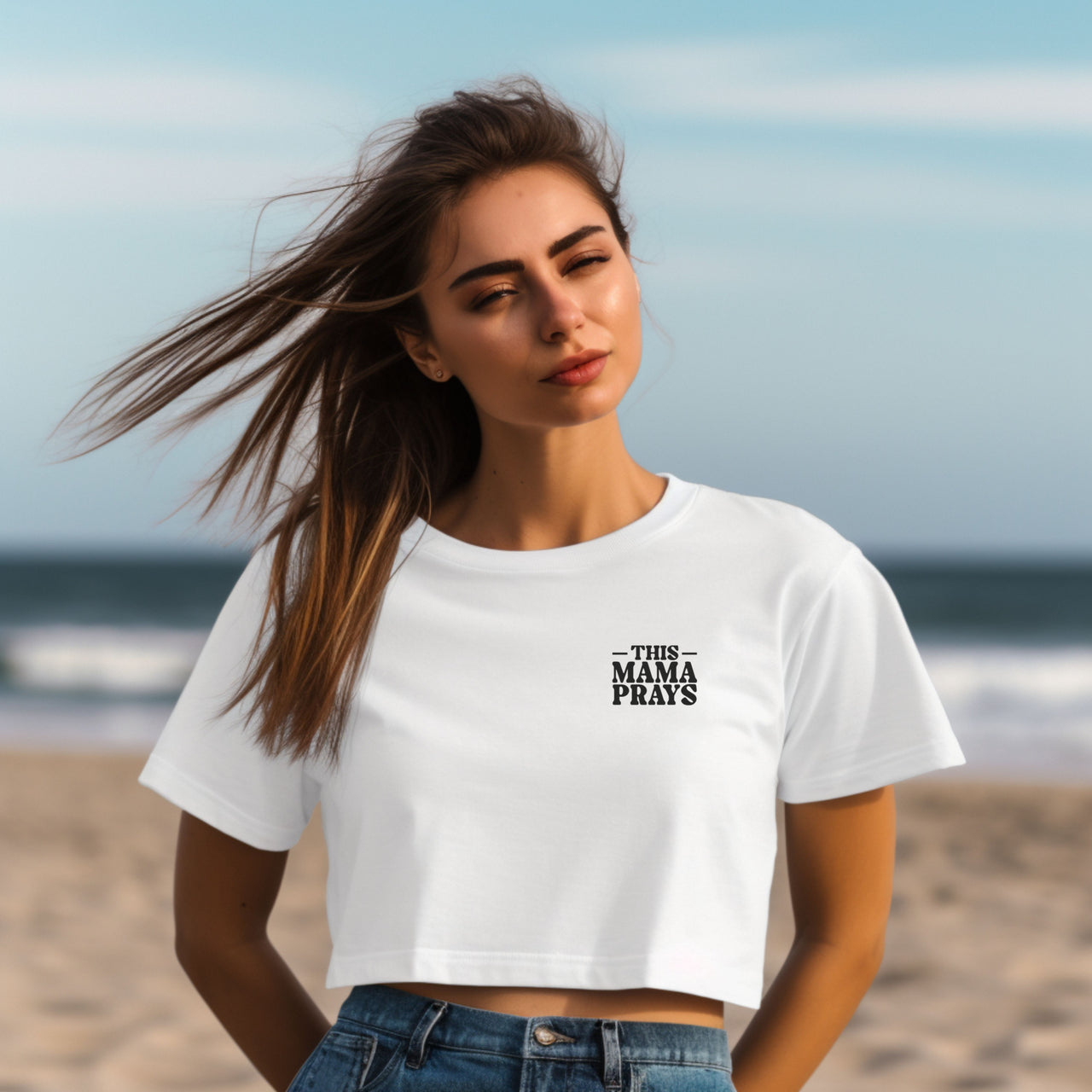 This Mama Prays Christian Crop Tee for Moms worn by a woman at the beach with wind-blown hair and a confident pose.