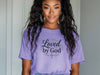 Woman wearing a violet Loved by God T-Shirt, showcasing a stylish and faith-inspired design for everyday wear.