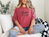 Woman sitting on a couch wearing a Loved by God T-Shirt, showcasing a comfortable and stylish design.